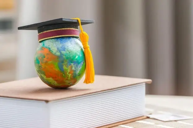 A globe wearing a graduation cap on top of a book