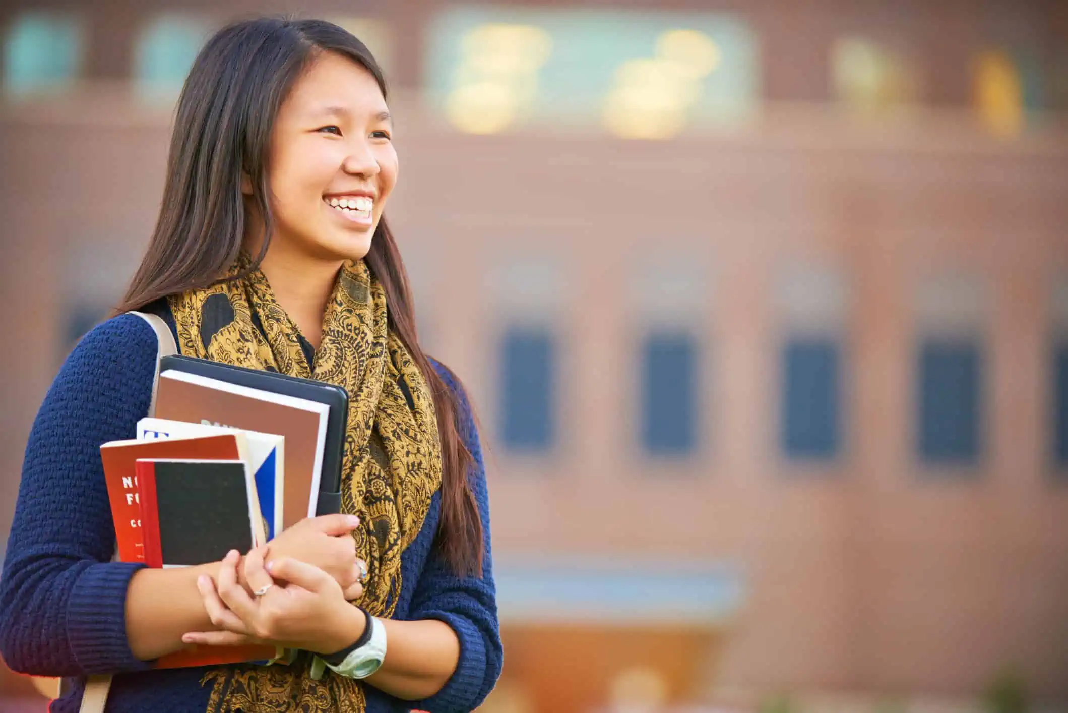 A young female student stands with her books on campus.