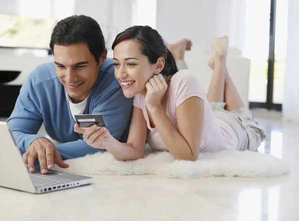 A couple look at a laptop together. The woman is holding a credit card.