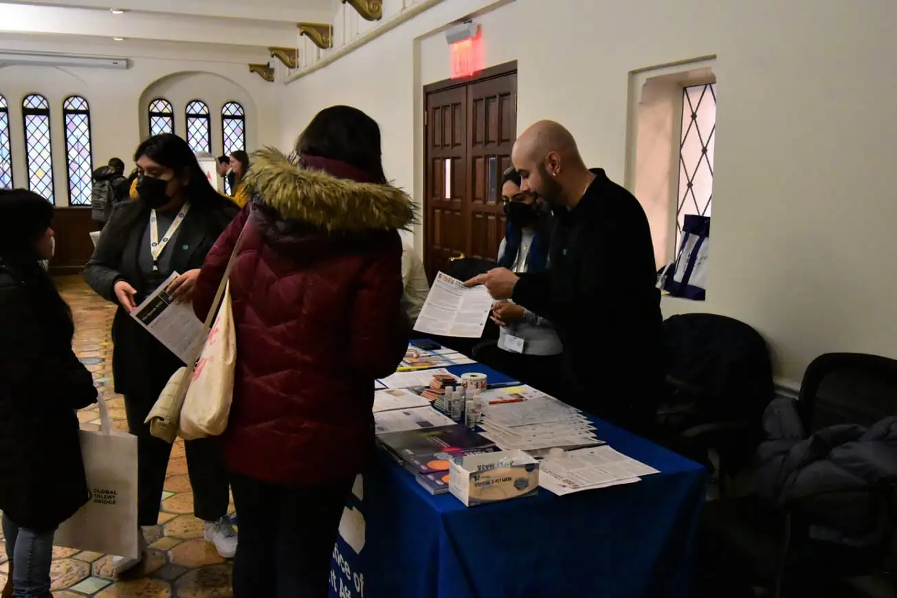 Representatives from immigrant- and refugee-serving initiatives handing factsheets to newcomers at an information fair.