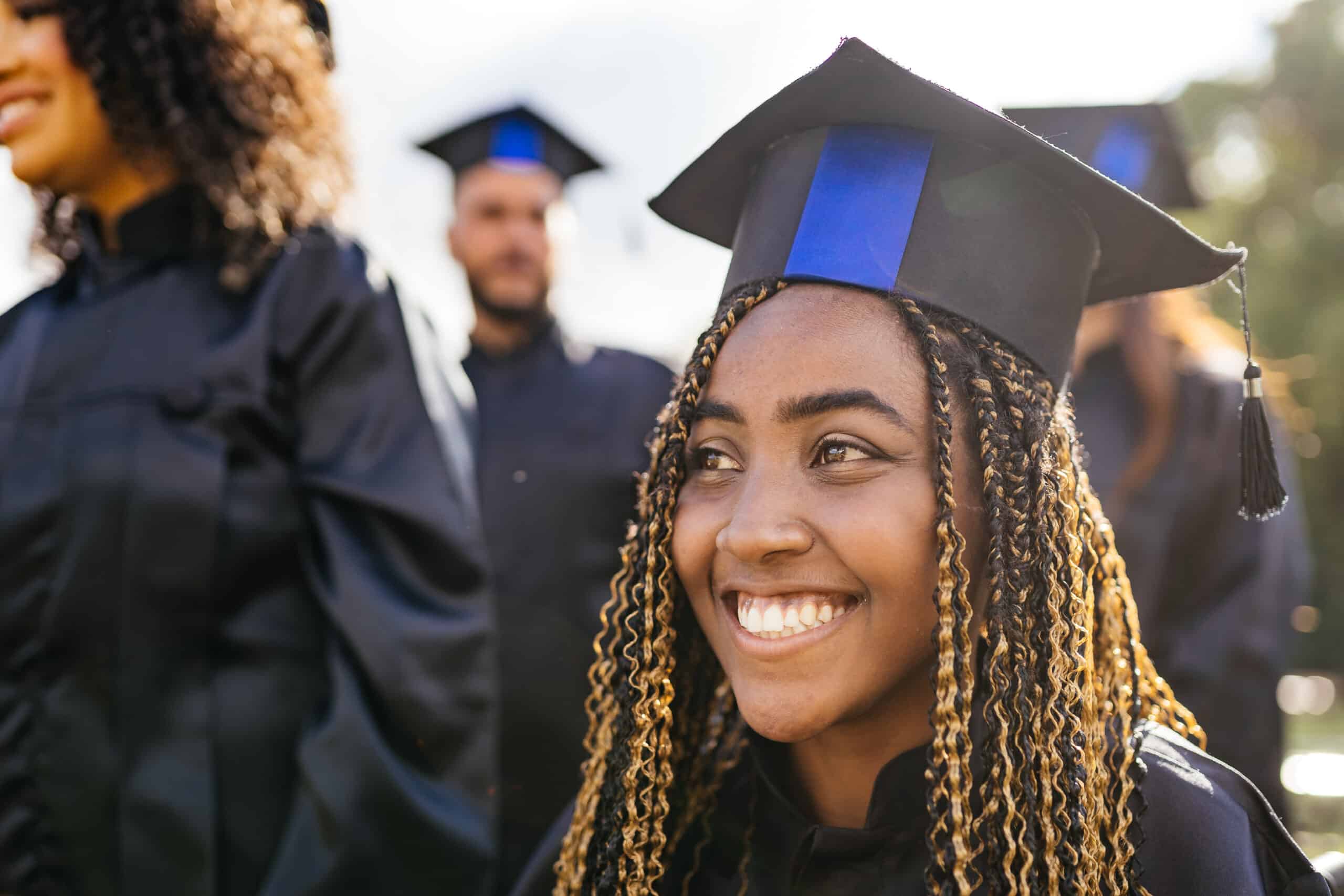 An African American graduate smiles big and is looking away from the camera.