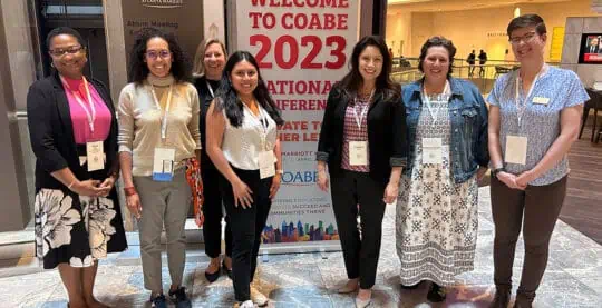 Six adults pose for group shot in front of COABE 2023 conference banner.